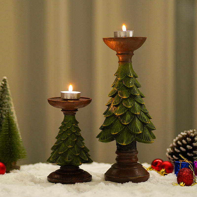 Two Christmas tree-shaped candle holders with candles on a snowy surface with decorative elements.