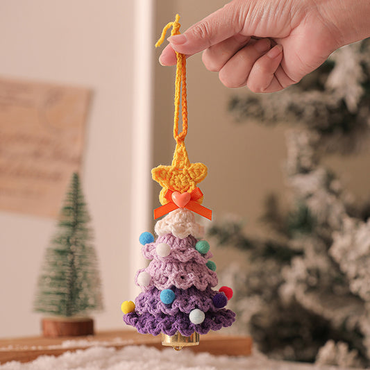 Hand holding a colorful crocheted Christmas tree ornament with a star on top, blurred Christmas tree in the background.